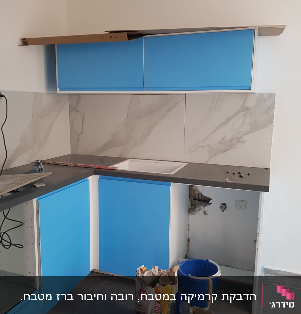 מטבח בשיפוץ עם ארונות כחולים, כיור ודלי צבע